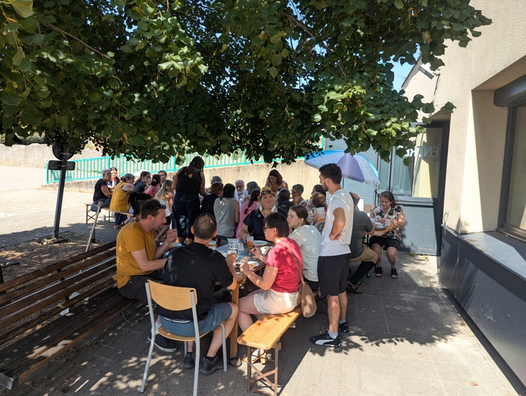 Participants attablés en extérieur sous les tilleuls devant la salle des fêtes